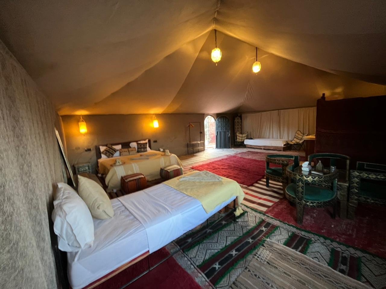 A ribbon of road winds through arid terrain toward distant golden dunes, the scenic overland journey that carries travelers from Morocco's cities to Merzouga.